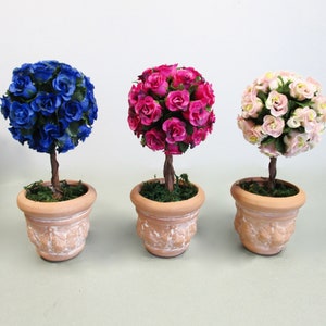 May include: Three potted topiary trees with artificial flowers. The trees are in terracotta pots with a whitewash finish. The flowers are blue, pink, and white.