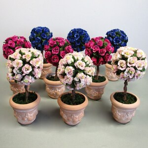 May include: A collection of miniature topiary trees in terracotta pots. The trees are decorated with pink, red, and blue paper roses.
