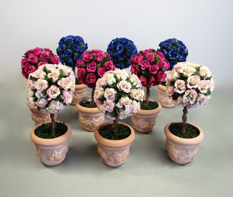 May include: A collection of miniature topiary trees in terracotta pots. The trees are decorated with pink, red, and blue paper roses.