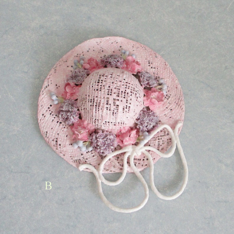 May include: A pink straw hat with a white ribbon and pink and purple flowers around the crown.