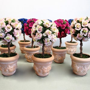 May include: A set of eight miniature topiary trees in terracotta pots. The trees are decorated with pink, red, and blue artificial flowers.
