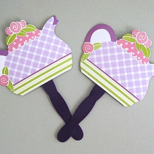 May include: Two purple and white teapot-shaped paper fans with green and pink floral accents. The fans have purple handles.