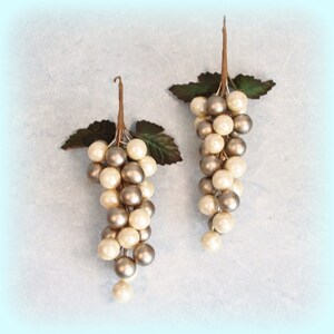 May include: Two decorative grape clusters with pearl-like beads in cream and silver. Each cluster has a brown stem and green leaves, creating a realistic appearance. Ideal for home decor or craft projects.