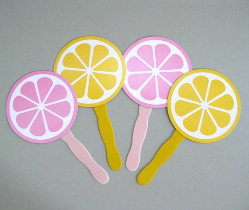May include: Four paper hand fans with yellow and pink lemon designs. The fans have white centers and are attached to wooden sticks.
