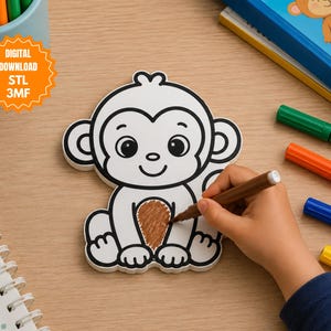 Op de afbeelding: Een witte aapvormige figuur met zwarte omlijningen en een bruin ingekleurd buikgedeelte. De figuur gaat vergezeld van een digitaal downloadlabel met de tekst DIGITAL DOWNLOAD STL 3MF, omringd door verschillende gekleurde stiften.