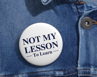 May include: White button with blue text that reads "NOT MY LESSON - To Learn -" on a denim background.