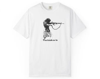 May include: White t-shirt featuring a black and white illustration of a person aiming a rifle. The person is wearing a jacket and skirt. The text "Tiocfaidh ár lá" is printed below the illustration.