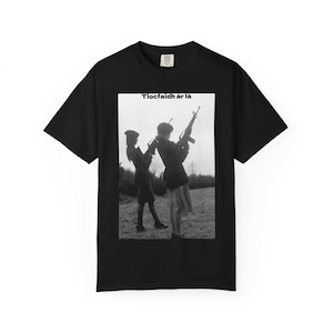 May include: Black t-shirt featuring a black and white image of two figures holding rifles, with the text "Tiocfaidh ár lá" above the image. The t-shirt is made of a soft material.