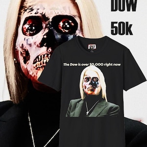 May include: Black t-shirt with a graphic of a person with a skull-like face, wearing a black turtleneck and blazer. The text "The Dow is over 50,000 right now" is printed on the shirt. The word "OBEY" is printed on the top of the shirt.