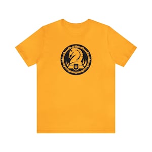 May include: A yellow t-shirt featuring a black knight chess piece logo. The logo is enclosed within a black circle with spikes.