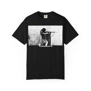 以下が含まれることがあります： ライフルを構える人物の白黒グラフィックが特徴の黒いTシャツ。グラフィックには白い文字で「Tiocfaidh ár lá」と書かれています。このシャツはクルーネックです。