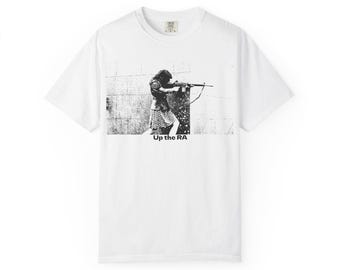 May include: White t-shirt featuring a black and white graphic of a person aiming a rifle. The graphic includes the text "Up the RA" at the bottom. The shirt has a crew neck and short sleeves.
