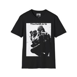 Könnte beinhalten: Schwarzes T-Shirt mit einer schwarz-weißen Grafik von maskierten Figuren, die eine Waffe halten. Der Text "Tiocfaidh ár lá" ist über dem Bild aufgedruckt. Das Shirt besteht aus einem weichen Material.