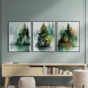 Könnte beinhalten: Drei Aquarelle, die eine Waldszene mit grünen und braunen Bäumen zeigen, die sich in einem stillen Gewässer spiegeln. Die Bilder sind in Schwarz gerahmt und an einer hellgrünen Wand über einem Holzregal aufgehängt.