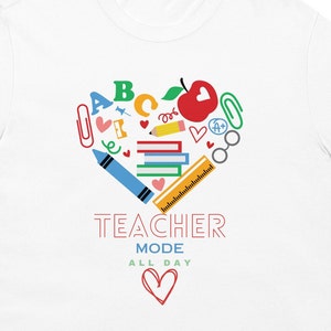 May include: White t-shirt with a red heart design filled with colorful school supplies, including an apple, crayons, pencils, and books. The text "TEACHER MODE ALL DAY" is printed below the heart.