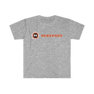 May include: A heather grey t-shirt with a white and orange logo. The logo is a circle with a black "K" in the center and the word "KOHO" written in orange below the circle.