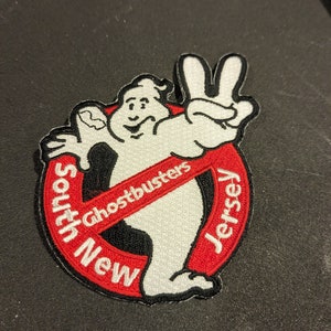 May include: Embroidered patch featuring the Ghostbusters logo with the Stay Puft Marshmallow Man. The patch is white, red, and black, with the words "South New Jersey" and "Ghostbusters" in a circular design.