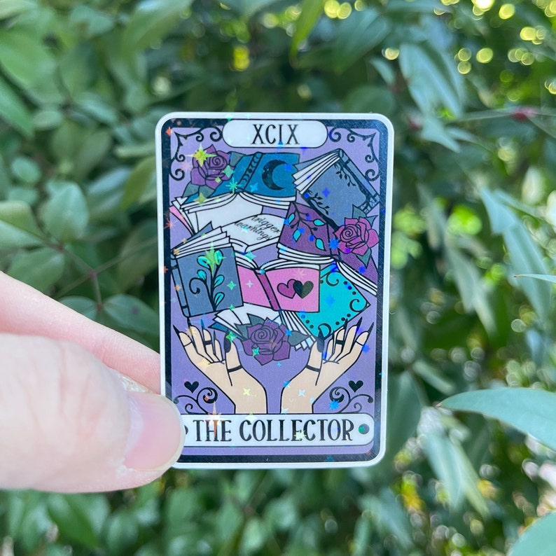 K&ouml;nnte beinhalten: Eine violette Tarotkarte mit holografischem Finish. Die Karte zeigt ein Paar H&auml;nde, die einen Stapel B&uuml;cher halten. Die Kartennummer ist XCIX und der Titel lautet "THE COLLECTOR".