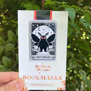 May include: Black and white bookmark featuring a mothman illustration with red eyes. The bookmark has the text "Mothman" and "Big Chair, Dreams" with the website "BigChairDreams.com".