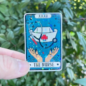 May include: A blue tarot card with a white nurse's hat, stethoscope, and syringe. The card is labeled "XXXII THE NURSE".