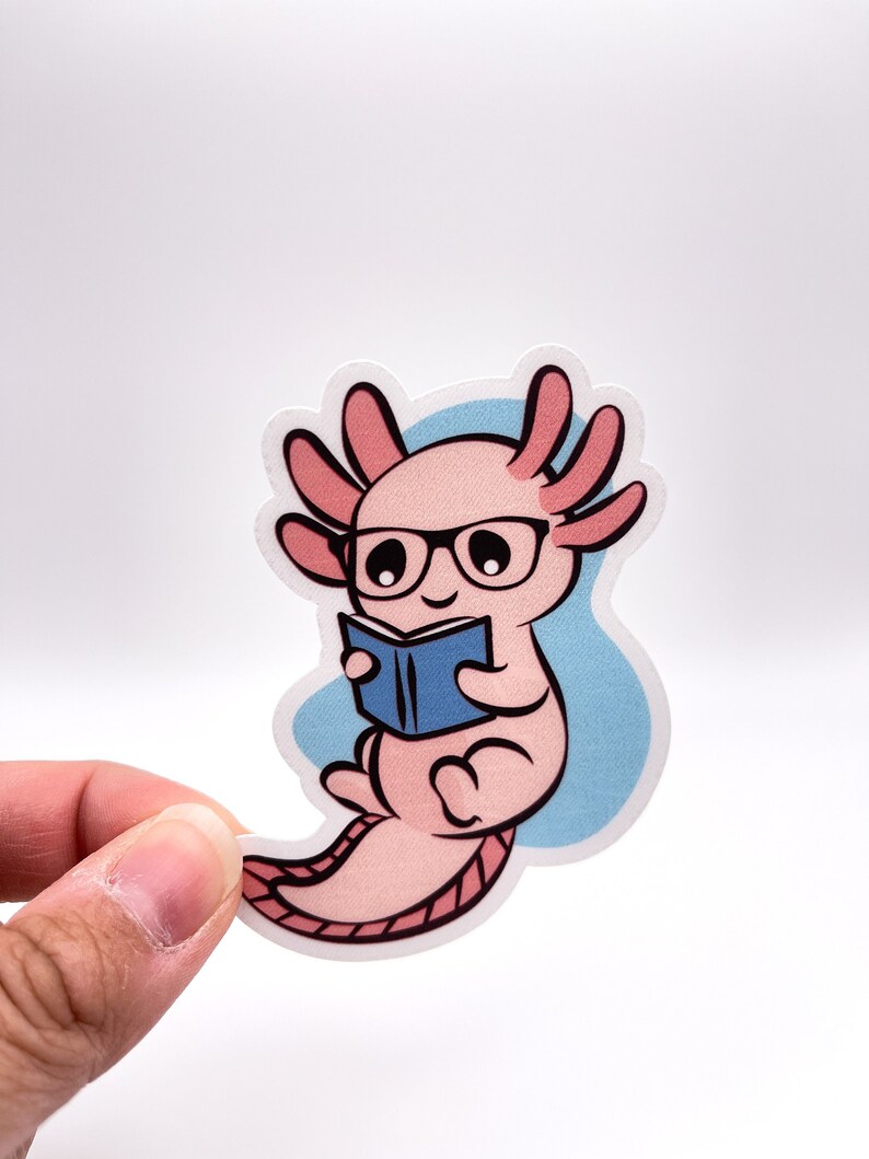 K&ouml;nnte beinhalten: Ein rosa Axolotl mit Brille, das ein blaues Buch liest. Das Axolotl sitzt auf einem hellblauen Hintergrund.