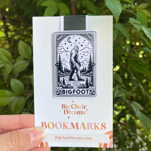 May include: Black and white illustration of Bigfoot walking through a forest with a crescent moon and stars in the sky. The bookmark is white with the text "Big Chair Dreams" and "BOOKMARKS" in a colorful font. The website address "BigChairDreams.com" is printed at the bottom.