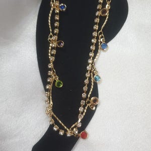 May include: Gold anklet with two chains and colourful gemstone charms. The anklet is displayed on a black card with the word "ANKLET" printed on it.