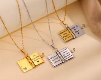 May include: Three open book pendant necklaces in gold and silver tones. Each pendant has a hinged design with engraved text and a small heart detail. The necklaces hang on delicate chains.