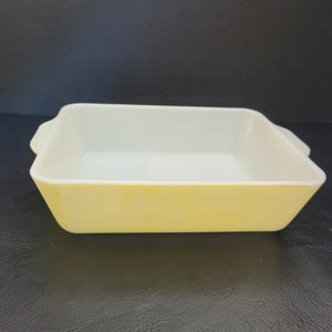 May include: A rectangular, yellow and white baking dish with two small handles. The dish has a yellow exterior and a white interior. The dish is made of glass and is suitable for baking.