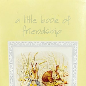 May include: A vintage book titled "a little book of friendship" with illustrations by Beatrix Potter. The cover features a light yellow background with a blue and white decorative border around a picture of two brown rabbits in a garden setting.