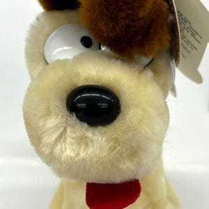 May include: A plush toy dog with brown ears, white fur, and a red tongue. The dog has large, white eyes and a black nose.