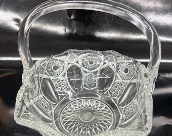 May include: A clear glass bowl with a handle, featuring a cut glass design. The bowl has a scalloped edge and a starburst pattern in the center.