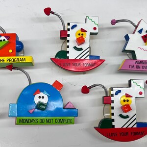 Może przedstawiać: Zestaw ośmiu kolorowych, geometrycznych drewnianych figurek z humorystycznymi powiedzeniami. Każda figurka ma inny wzór i inne powiedzenie. Powiedzenia obejmują "Get with the program", "I love your format", "Warning I'm on overload", "Mondays do not compute".