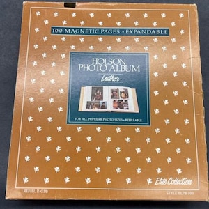 May include: A brown box with a gold pattern and the text "Holson Photo Album Leather" on the front. The box is for a photo album that holds 100 magnetic pages and is expandable. The box also says "For all popular photo sizes. Refillable" and "Elite Collection Style ELPB-100".