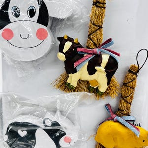 May include: Four farmhouse-themed ornaments featuring a cow, pig, and two different styles of cow heads. The ornaments are made of painted wood and have a straw-like texture.