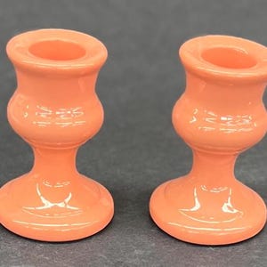 Pode incluir: Dois castiçais de cerâmica cor coral. Cada castiçal tem uma base larga e uma parte superior estreita com uma abertura circular.