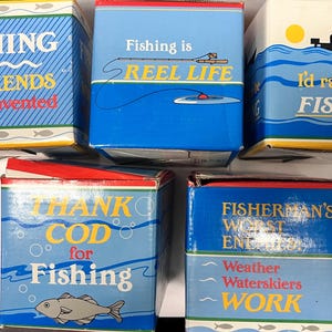 May include: Five colourful boxes with fishing-themed sayings. The boxes are blue, red and yellow with white lettering. The sayings include "Fishing is why weekends were invented", "Fishing is reel life", "I'd rather be fishing", "Thank cod for fishing", and "Fisherman's worst enemy: weather, waterskiers, work".