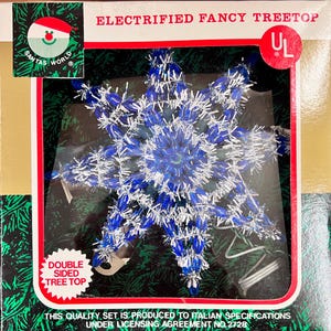Puede incluir: Adorno de árbol de Navidad eléctrico en forma de copo de nieve azul y plateado. El texto «ELECTRIFIED FANCY TREETOP» aparece en el embalaje. El producto es de doble cara. También se puede leer «SANTAS WORLD» y «DOUBLE SIDED TREE TOP».