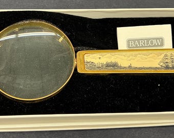 May include: A gold-toned magnifying glass with a handle that features a small, framed image of a ship sailing on the water. The handle is labeled "Barlow".