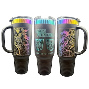 May include: Three black stainless steel tumblers with a rainbow iridescent finish. The tumblers feature a graphic of the Transformers characters Soundwave and Blaster. The text "Transformers" and the Autobot symbol are also featured on the tumblers.