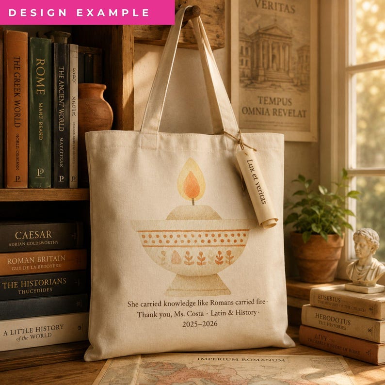 May include: A beige canvas tote bag featuring a printed illustration of a lit oil lamp. Below the lamp, the text reads: She carried knowledge like Romans carried fire - Thank you, Ms. Costa - Latin & History - 2025-2026. A small paper tag attached to the handle says Lux et veritas.