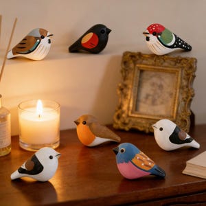 May include: A collection of seven small, hand-painted wooden bird figurines featuring various colour patterns including brown, black, red, green, white, blue, and pink. Each bird has a smooth, rounded shape with painted eyes and distinct markings.