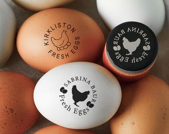 May include: A collection of brown and white eggs, some stamped with black ink designs featuring a chicken silhouette and the text KIRKLISTON FRESH EGGS or SABRINA BAUR FRESH EGGS, alongside a round black stamp with a white chicken graphic.