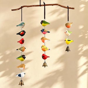 Könnte beinhalten: Dekorative Mobile mit handbemalten Holzvögeln, die an einem natürlichen Ast hängen. Die Vögel sind in verschiedenen Farben gehalten, darunter Rot, Gelb, Blau und Grün. Einige Vögel haben kleine Messingglocken. Für den Innenbereich.