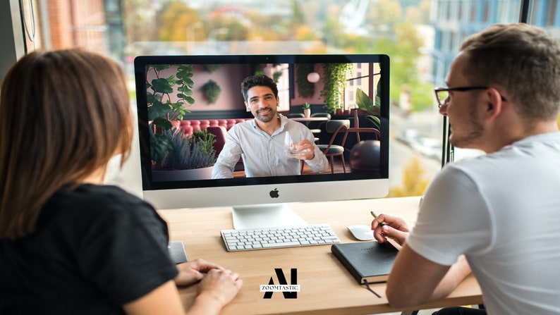 May include: Two people are having a video call on a computer. The person on the screen is sitting in a restaurant and holding a glass of water. The person on the left is looking at the screen, while the person on the right is looking at the screen and holding a pen.