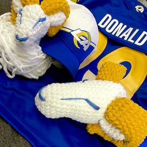 May include: Two crocheted ram head ornaments in white and yellow, with blue accents, on a blue and yellow football jersey with the name "DONALD" on the back.