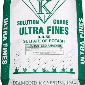Op de afbeelding: Een witte zak Diamond K Ultra Fines 0-0-50 sulfaat van potas meststof met groene zijpanelen. De voorzijde bevat een diamantlogo, tekst met de gegarandeerde analyse en een afbeelding van regen die op kleine groene planten valt.