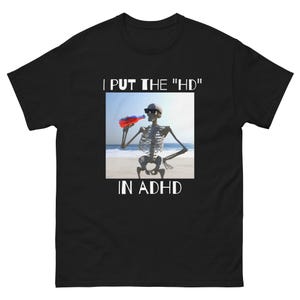 Könnte beinhalten: Schwarzes T-Shirt mit einer weißen Grafik eines Skeletts mit Sonnenbrille, das aus einer rot-blauen Dose trinkt. Der Text "I PUT THE "HD" IN ADHD" ist in Weiß auf das Shirt gedruckt.