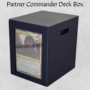 May include: A black Partner Commander Deck Box with a card visible in a clear window. The box has a textured top and a handle. Text at the top reads "Partner Commander Deck Box". The card features a character named "Sam, Loyal Attendant".