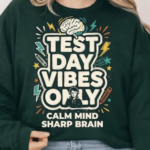May include: Dark green sweatshirt with the text "TEST DAY VIBES ONLY" in white, with a brain graphic and lightning bolts. The phrase "CALM MIND SHARP BRAIN" is printed below the main text. A pencil and star graphics are also included.